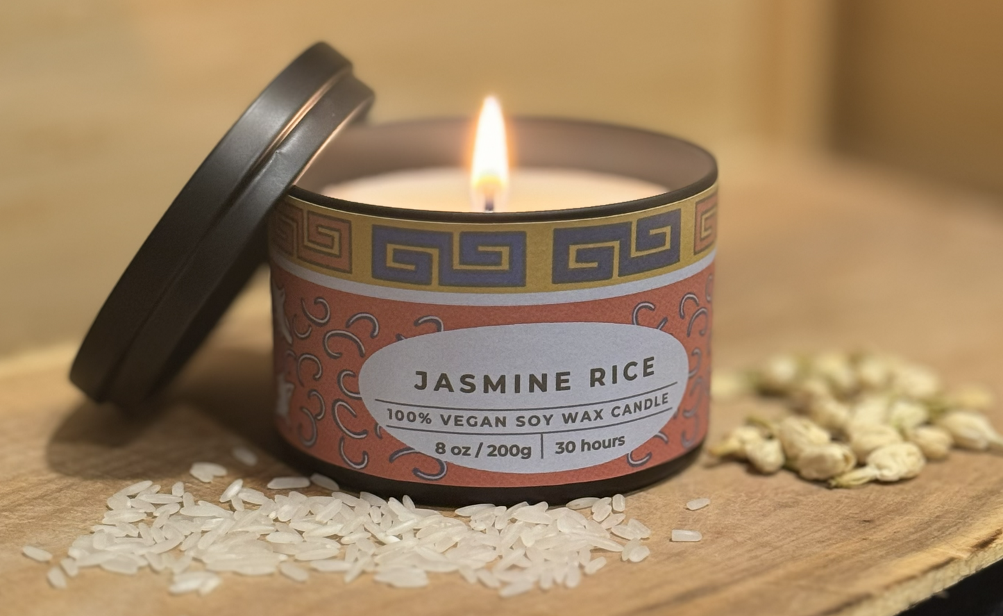 Candle labeled 'Jasmine Rice' with a lit wick on a wooden surface with rice grains.