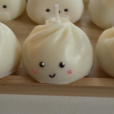 Candle shaped like bao (steamed bun) with faces on a wooden tray.