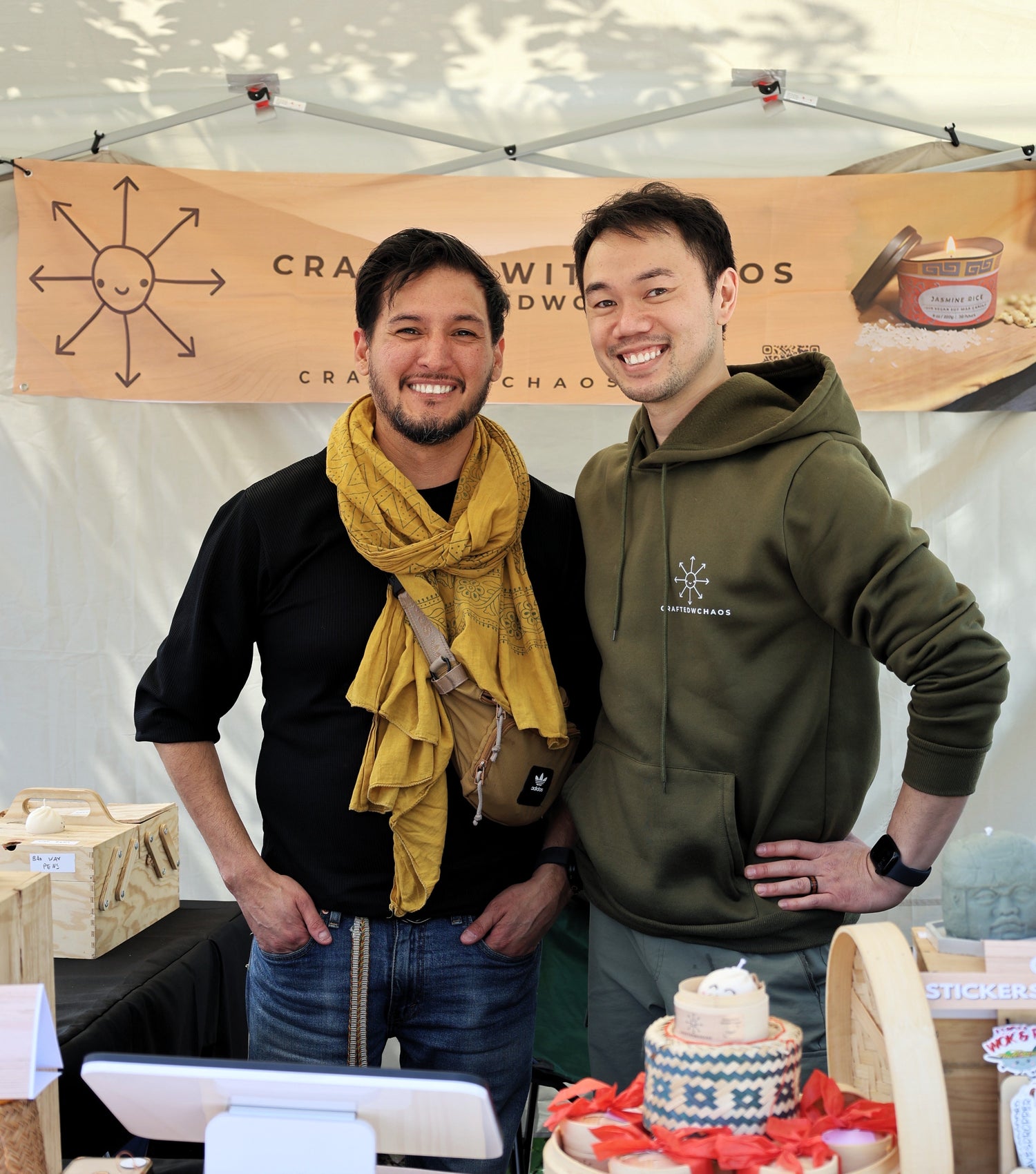 Two men standing behind a table with products at an event, under a banner reading 'Craft with Chaos'.